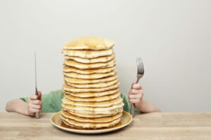 a person holding a fork and knife in front of a stack of pancakes