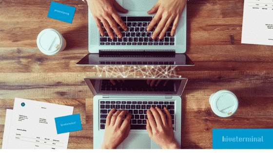 two people typing on their laptops on a wooden table