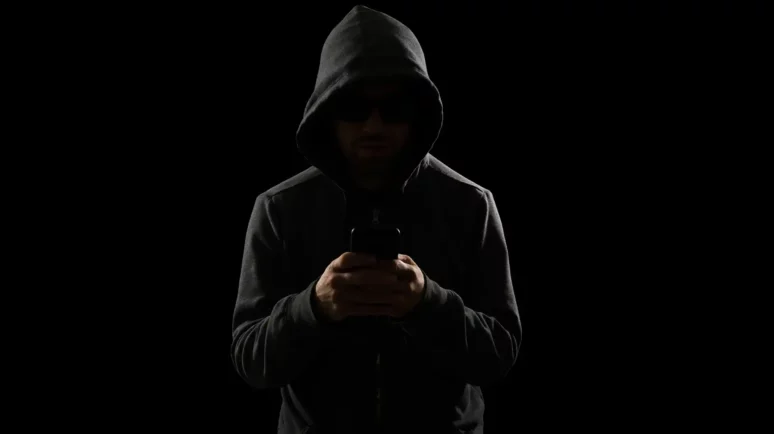Suspicious man in a hoodie on his phone, dark room.