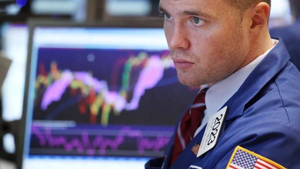 Stock trader looking at computer. Stock market chart/data in background.