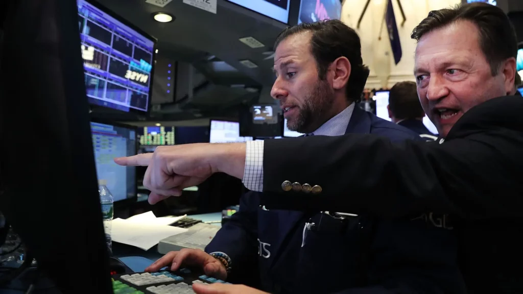 Two Wall Street traders looking at computer, one pointing aggressively towards it.
