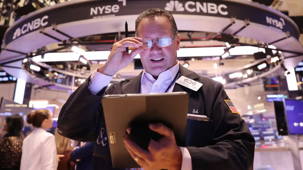 Wall street stock trader adjusting his glasses looks down at hand held computer device.