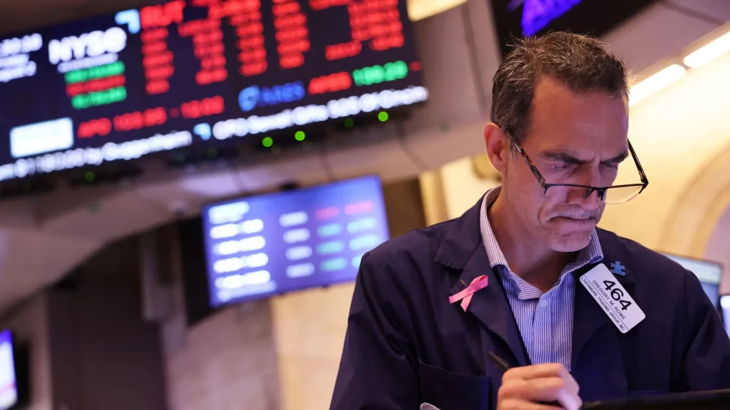 New York Stock Exchange trader, red figures on exchange board in background.
