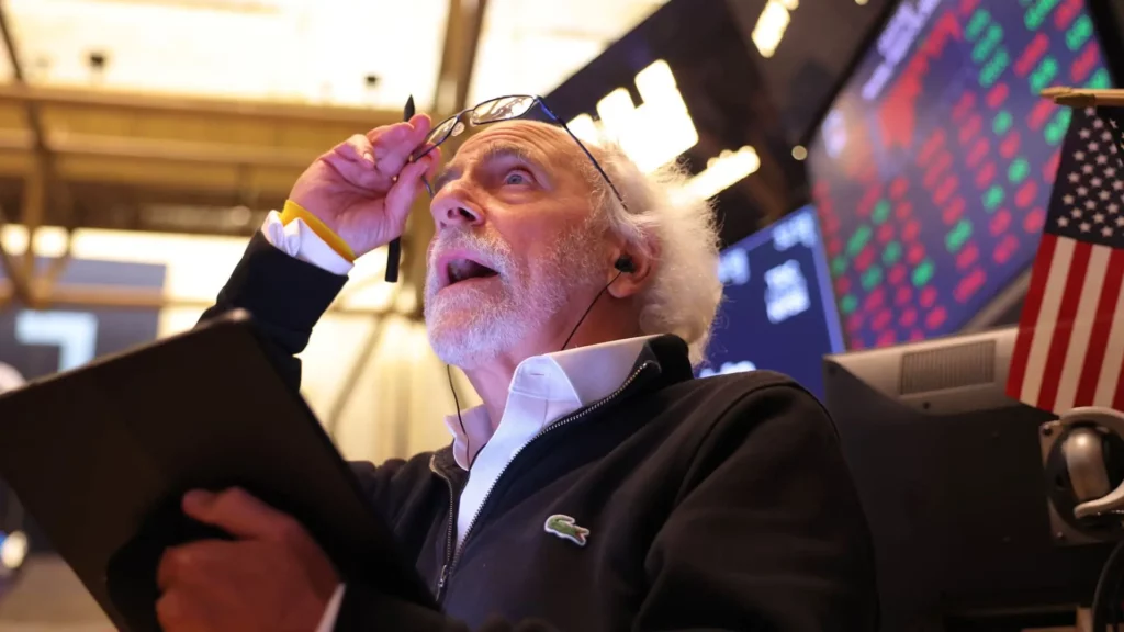 U.S. stock trader adjusting glasses, looking up at trading data.