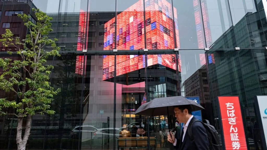 A man walks past a building with a large stock price display board in Tokyo, Japan